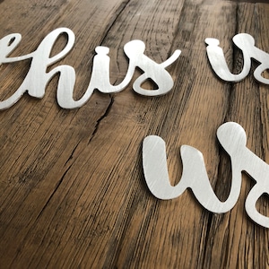 May include: Silver metal letters spelling out "this is us" on a rustic wooden background.