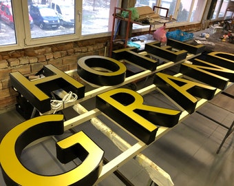 Pode incluir: Uma grande placa tridimensional que lê "HOTEL GRAND" em letras douradas com contornos pretos. As letras são montadas em uma moldura de madeira.