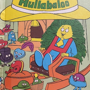 May include: A children's book cover featuring a yellow hat with the text "Hat Helpers Hullabaloo". The cover also features a green-haired character sitting in a rocking chair with a red letter "H" on their chest.