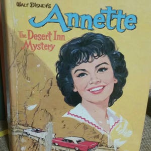May include: A vintage paperback book cover featuring a young woman with dark hair and a bright smile. The book title is "Annette The Desert Inn Mystery" and is attributed to Walt Disney's.