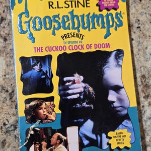 May include: A vintage Goosebumps book titled "The Cuckoo Clock of Doom" by R.L. Stine. The cover is yellow and blue with images from the TV show. The book is a Scholastic publication and includes color photos.