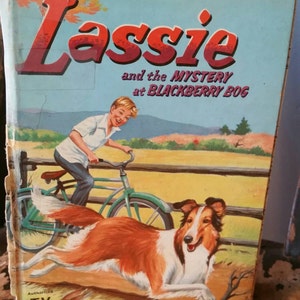 May include: A vintage book cover featuring a colorful illustration of a boy riding a bicycle with a Collie dog running alongside. The book title is "Lassie and the Mystery at Blackberry Bog" with the words "TV Edition" at the bottom.