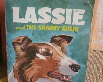 May include: A vintage paperback book cover featuring a close-up of a brown and white Collie dog with the title "Lassie and The Shabby Sheik" in white text on a turquoise background.