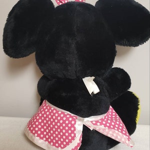 May include: A black plush toy with large ears and a pink polka dot bow. The toy is wearing a pink and white polka dot skirt. The toy is sitting down.