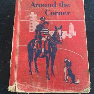 May include: Red book cover with the title "Around the Corner" in blue lettering. The cover features an illustration of a police officer on horseback with a child riding behind him. A small dog is sitting in the foreground.