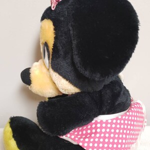 May include: A plush Minnie Mouse doll, featuring black fur, a yellow muzzle, and a pink polka-dot skirt. A pink bow adorns the top of the head. The doll is in a seated position, showcasing its classic design.