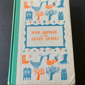 May include: A vintage hardcover book with a white cover and blue and orange illustrations. The title is "Hans Brinker or the Silver Skates".