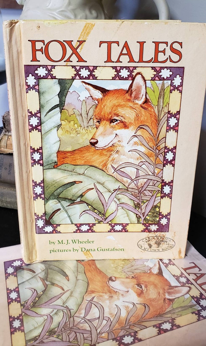 May include: A vintage children's book titled "Fox Tales" by M.J. Wheeler with illustrations by Dana Gustafson. The cover features a red fox sitting in a lush green jungle setting.