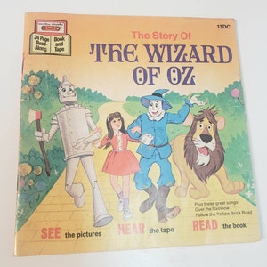 May include: A vintage children's book cover featuring illustrations of Dorothy, the Scarecrow, the Tin Man, and the Cowardly Lion from the classic story "The Wizard of Oz". The cover is yellow with a red brick road and green foliage. The book includes a 24-page read-along tape.