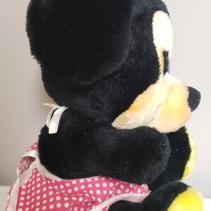 May include: A plush Minnie Mouse doll, primarily black with yellow accents on the feet and face. She wears a pink polka-dot dress and a matching bow. The doll is soft and cuddly, perfect for children.