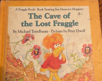 May include: A Fraggle Rock book cover featuring a yellow Fraggle with red hair and a red shirt, looking thoughtful. The book title is "The Cave of the Lost Fraggle" by Michael Teitelbaum with illustrations by Peter Elwell.