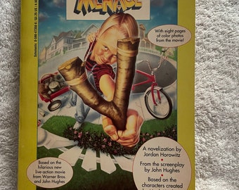 May include: A yellow paperback book cover with a picture of a boy holding a slingshot. The book title is "Dennis the Menace" and the text on the cover says "Based on the hilarious new live-action movie from Warner Bros. and John Hughes".