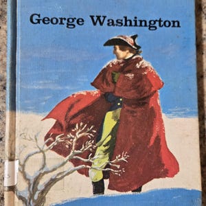 May include: A vintage book titled "George Washington" by Clara Ingram Judson. The cover features an illustration of George Washington in a red coat against a snowy backdrop. The book has a blue cover with white text.