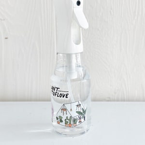 May include: White plastic spray bottle with a clear liquid inside. The bottle has a label with the text "Plant to Love" and a graphic of a greenhouse with plants.