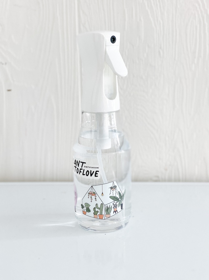 May include: White plastic spray bottle with a clear liquid inside. The bottle has a label with the text "Plant to Love" and a graphic of a greenhouse with plants.