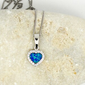 May include: A silver chain necklace with a blue opal heart pendant surrounded by clear cubic zirconia stones.