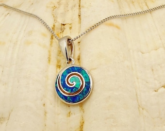 Könnte beinhalten: Eine silberne Halskette mit einem blauen und grünen Opal-Anhänger mit Spiraldesign. Der Anhänger befindet sich auf einem weißen Muschelhintergrund.