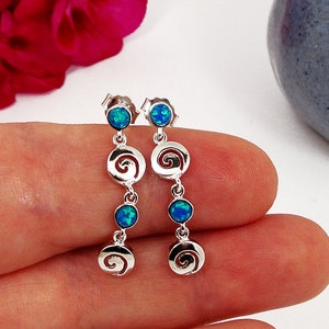 Könnte beinhalten: Silberne Ohrhänger mit blauen Opal-Steinen und einem Spiral-Design.