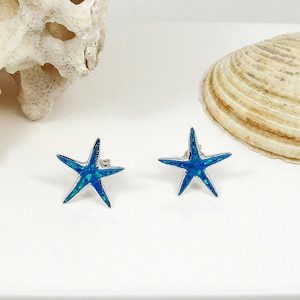 Puede incluir: Un par de pendientes de estrella de mar de ópalo azul. Los pendientes son de plata y tienen una incrustación de ópalo azul.