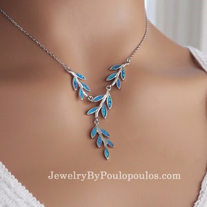 Könnte beinhalten: Eine silberne Halskette mit einem zarten Design aus blauen Opalblättern. Die Halskette verfügt über einen V-förmigen Anhänger mit kaskadierenden Blättern, die einen fließenden und eleganten Look erzeugen. JewelryByPoulopoulos.com