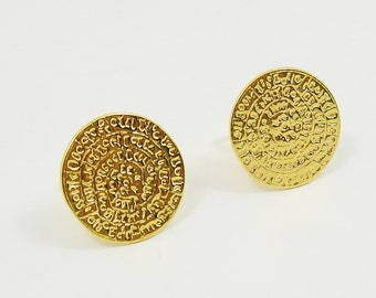 May include: A pair of gold-toned earrings with a circular design featuring intricate patterns. The earrings are made of metal and have a textured surface.