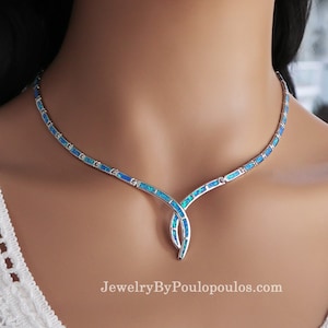 May include: A silver necklace with blue opal inlays. The necklace has a curved design with a central pendant. The website address "JewelryByPoulopoulos.com" is visible at the bottom of the image.