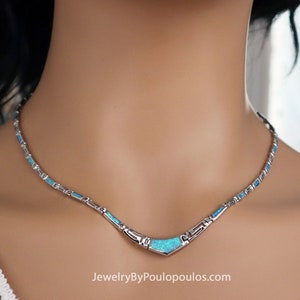 May include: A silver necklace with a blue opal pendant. The necklace has a delicate chain with small blue opal accents. The pendant is a curved shape with a smooth, polished surface. The necklace is a beautiful and elegant piece of jewelry.
