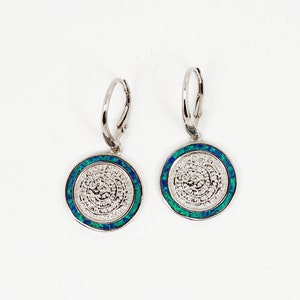 May include: A pair of silver hoop earrings with a round, white, textured design surrounded by a blue and green border.