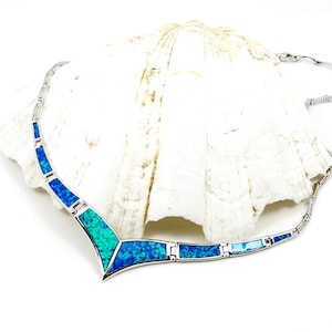 Puede incluir: Un collar de plata con un colgante en forma de V engastado con piedras de ópalo azul y verde.