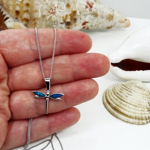 Puede incluir: Un collar de plata con un colgante de lib&eacute;lula con detalles de &oacute;palo azul. La lib&eacute;lula es un s&iacute;mbolo popular de transformaci&oacute;n y cambio.
