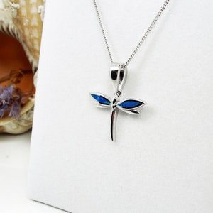 Puede incluir: Un collar con un colgante de lib&eacute;lula de plata con detalles de &oacute;palo azul. El collar est&aacute; sobre un fondo blanco.