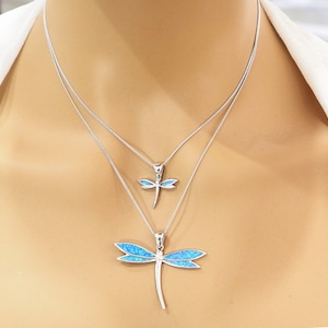 Puede incluir: Un collar de plata con dos colgantes de lib&eacute;lula. El colgante m&aacute;s grande es de &oacute;palo azul y el m&aacute;s peque&ntilde;o es de &oacute;palo transparente.