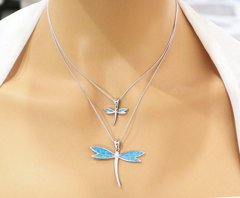 Puede incluir: Un collar de plata con dos colgantes de lib&eacute;lula. El colgante m&aacute;s grande es de &oacute;palo azul y el m&aacute;s peque&ntilde;o es de &oacute;palo transparente.