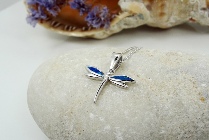 Puede incluir: Collar con colgante de lib&eacute;lula de plata con detalles de &oacute;palo azul. La lib&eacute;lula es un s&iacute;mbolo popular de transformaci&oacute;n y cambio.