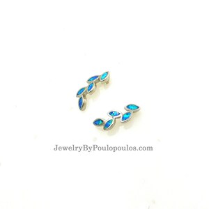 Op de afbeelding: Twee zilveren oormanchetten met een rij blauwe opaalstenen in de vorm van bladeren. De oormanchetten zijn gebogen en hebben een delicaat ontwerp. JewelryByPoulopoulos.com