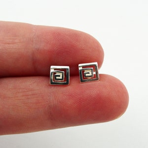 Puede incluir: Un par de pendientes de plata con un diseño cuadrado que presenta un patrón de espiral.