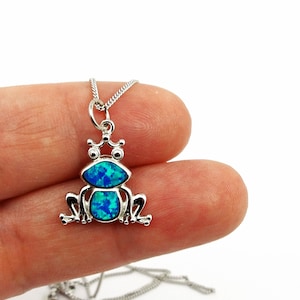 Puede incluir: Un collar de cadena de plata con un colgante de rana de ópalo azul.