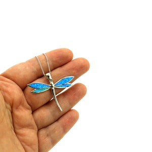 Puede incluir: Un collar con un colgante de lib&eacute;lula de plata con alas de &oacute;palo azul. El colgante est&aacute; en una cadena de plata.