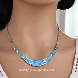 May include: A silver necklace with a crescent-shaped design featuring blue opal stones. The necklace is on a white mannequin.