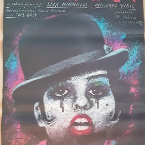 May include: A vintage movie poster for "Kabaret" featuring Liza Minnelli. The poster has a black background with the film's title in red and white text. The image shows a stylized portrait of a person wearing a top hat and makeup.