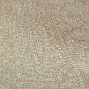 Puede incluir: Primer plano de una tela beige con un patr&oacute;n floral blanco. La tela tiene un patr&oacute;n de cuadr&iacute;cula sutil.