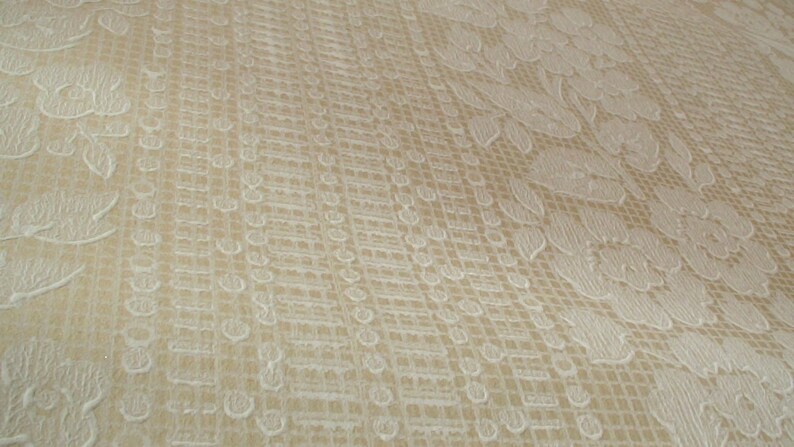 Puede incluir: Primer plano de una tela beige con un patr&oacute;n floral blanco. La tela tiene un patr&oacute;n de cuadr&iacute;cula sutil.