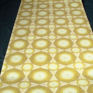 May include: A close-up of a wallpaper roll with a repeating pattern of white and yellow circles with a geometric design. The wallpaper has a vintage look and feel.
