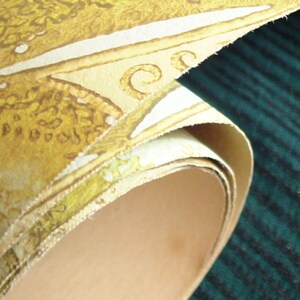 May include: A roll of yellow wallpaper with a white and brown pattern. The wallpaper is rolled up and the end of the roll is visible. The wallpaper is on a dark green surface.
