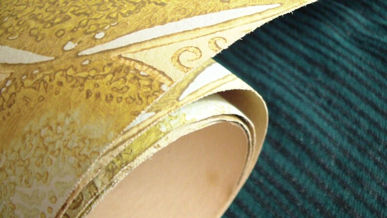 May include: A roll of yellow wallpaper with a white and brown pattern. The wallpaper is rolled up and the end of the roll is visible. The wallpaper is on a dark green surface.