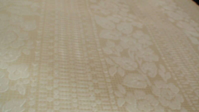 Puede incluir: Primer plano de una tela blanca con un sutil patr&oacute;n floral en relieve. La tela tiene una superficie ligeramente texturizada.
