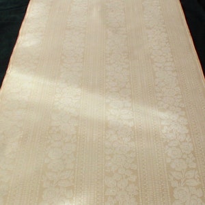 Puede incluir: Primer plano de una tela blanca con un sutil estampado floral y rayas verticales. La tela tiene una superficie suave y texturizada.