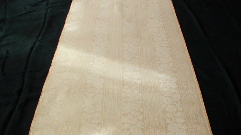 Puede incluir: Primer plano de una tela blanca con un sutil estampado floral y rayas verticales. La tela tiene una superficie suave y texturizada.