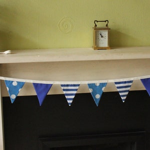 May include: A blue and white bunting with a variety of patterns, including stripes and polka dots, hangs above a fireplace.