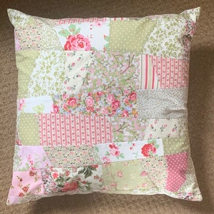 May include: A patchwork pillow with a floral design in shades of pink, green, and white. The pillow is made of different fabrics and has a quilted look.